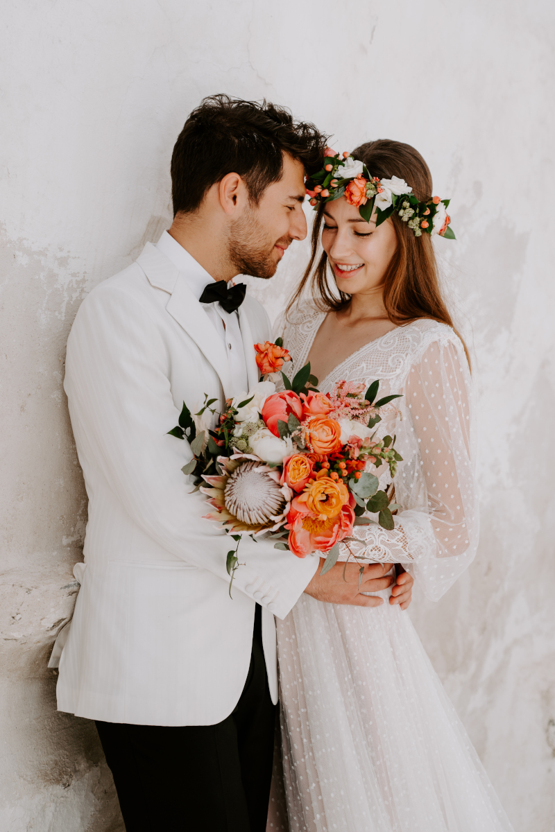 A wedding couple in Mykonos in elegant white attire, the bride in a wedding dress and the groom in a white tuxedo.