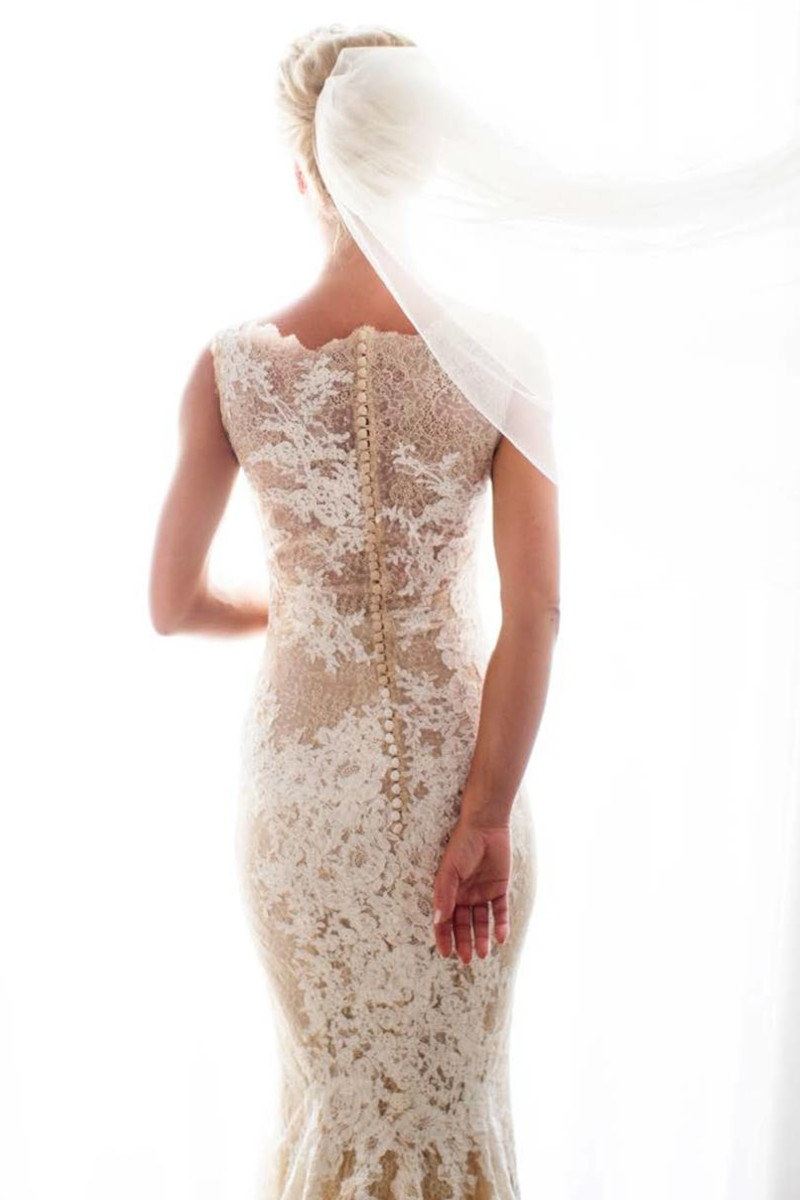 A bride in a wedding gown stands gracefully before a window, envisioning her dream destination wedding in Mykonos.