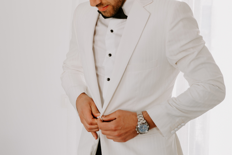 A stylish man in a white suit adjusts his tie, preparing for an event party in Mykonos.