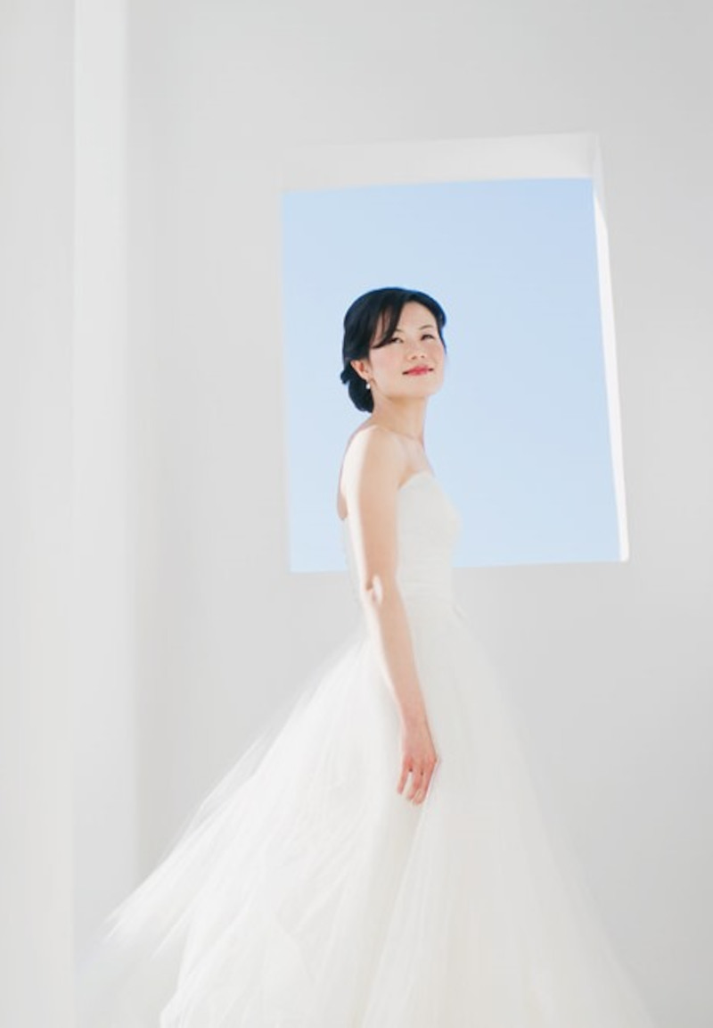 An enchanting bride in a white dress, poised before a window, exuding timeless elegance in this Mykonos wedding.
