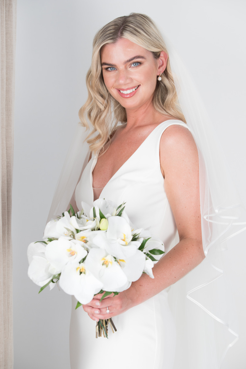 Gorgeous bride in white wedding dress and a veil holding a white bridal bouquet in Mykonos for her wedding.