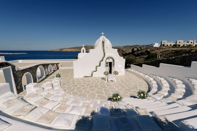 A wedding ceremony set up in Mykonos with a white church and a view of the ocean decorated with flower garlands