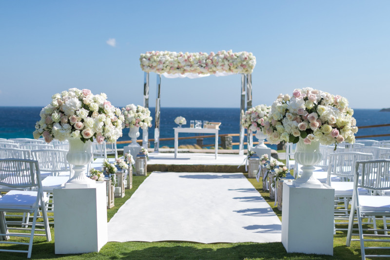 A picturesque outdoor wedding ceremony featuring white chairs and a stunning floral arrangement, luxury wedding in Mykonos