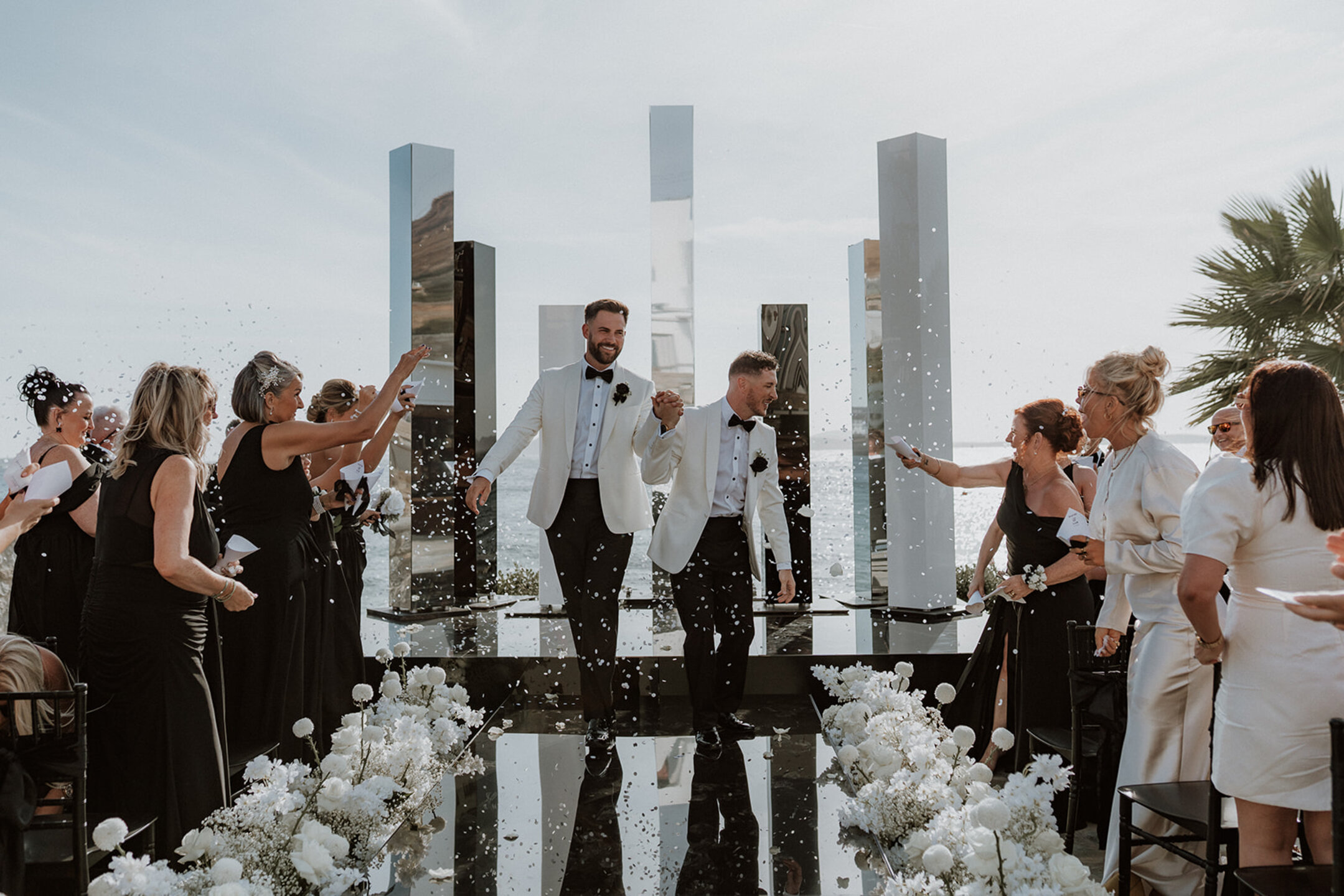 Same-sex weddings in Mykonos with grooms walking down a mirrored ceremony aisle and bespoke modern wedding decoration at an exclusive Greek island venue